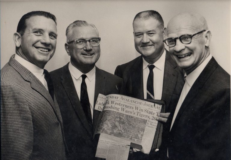 1939 Lubbock State Champion Football Team reunion: four men hold a newspaper clipping on beating Waco's Tigers