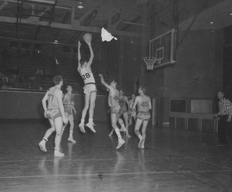 1951 Lubbock State Championship Basketball Team player leaping for a jump shot as defenders look on in a gym