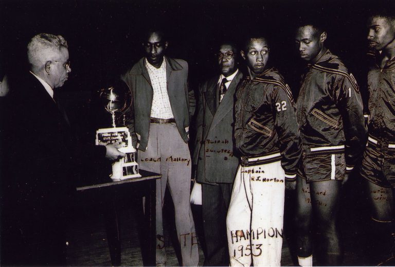 1953 Dunbar State Championship Basketball Team players and coach viewing the state championship trophy on a table