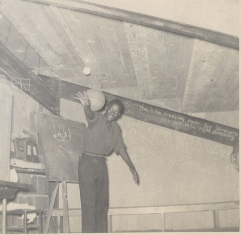 Man reaching up with a basketball in a dressing room, from the 1957 Dunbar State Championship Basketball Team