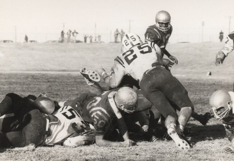 1968 Estacado Matadors Football game action with a player in a white number 25 jersey stepping over a pile of players