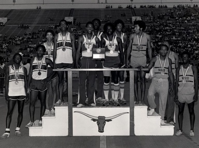1983 Estacado High School Boys Track and Field State Champions relay medalists with batons and a plaque on a longhorn podium