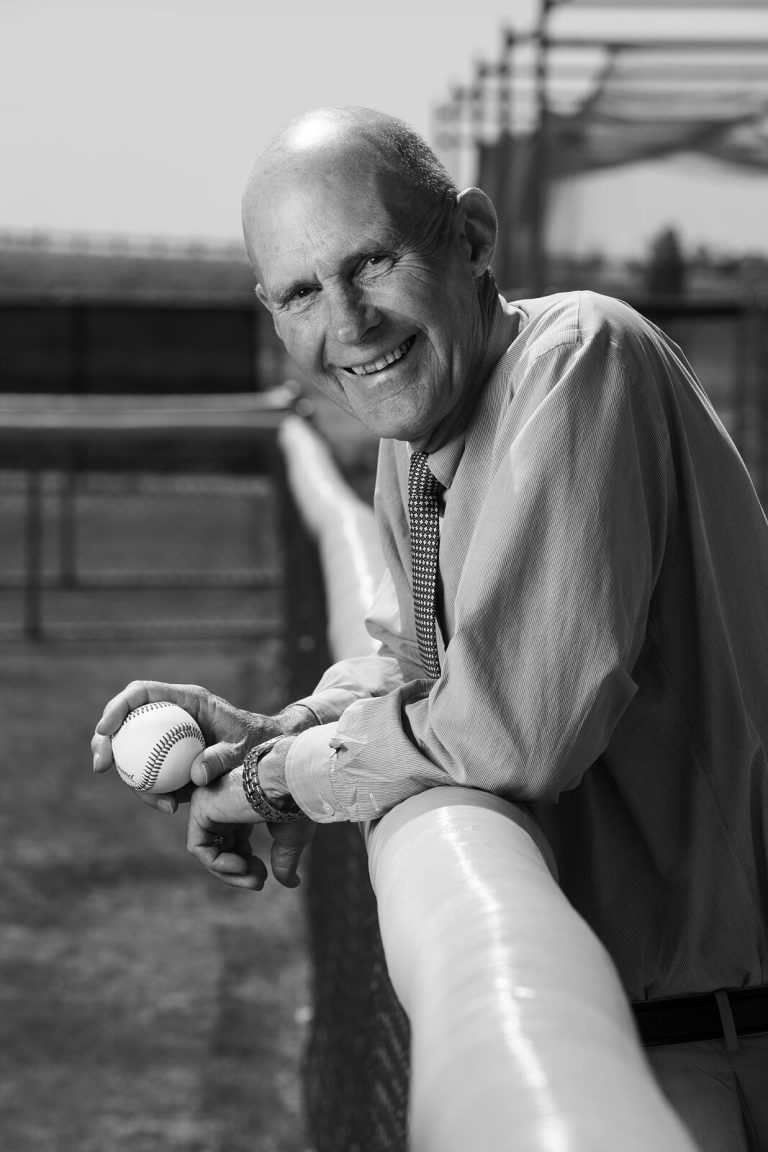 Bill Dean smiling and leaning on a padded rail while holding a baseball, black-and-white portrait