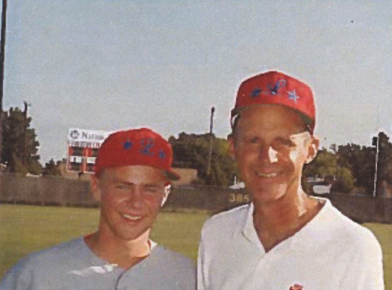 Bill Dean smiling beside a young player, both in red caps with blue stars, on a baseball field