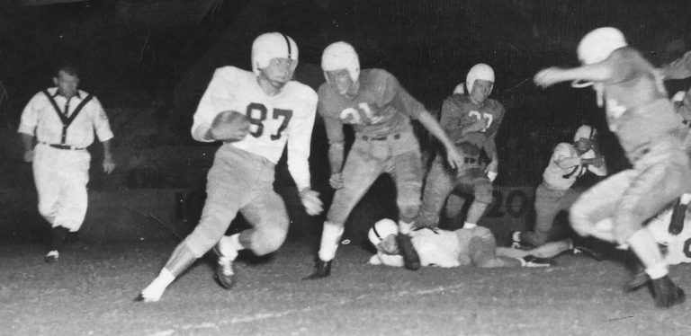 Bobby Brown in number 87 running with the ball in a night football game, black and white