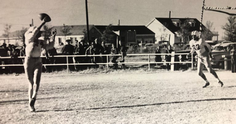 Bobby Brown throwing a pass in a football game with spectators lined along the sideline, black and white