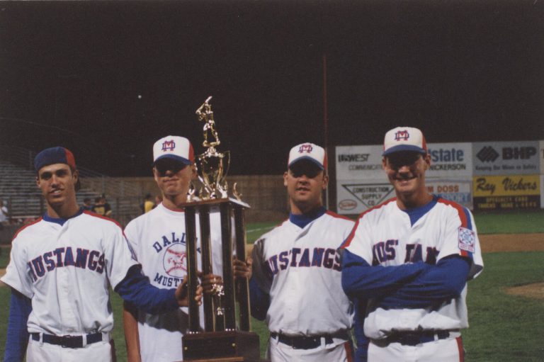 Brad Ralston and Mustangs teammates posing with a large trophy at a ballpark at night