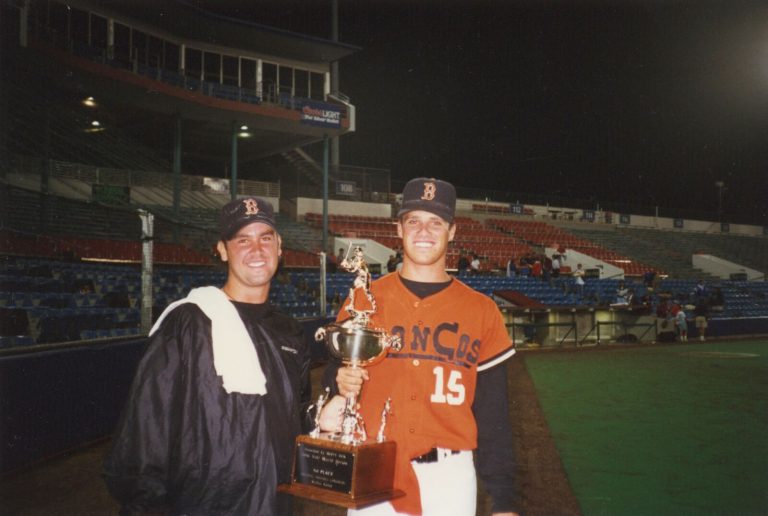 Brad Ralston and a teammate with a first-place trophy at a Cape Cod summer league ballpark at night