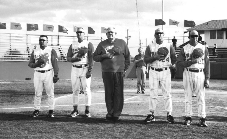 Cal Lowry lined up on the field with four Coronado Mustangs baseball players in pinstripes, caps held over hearts