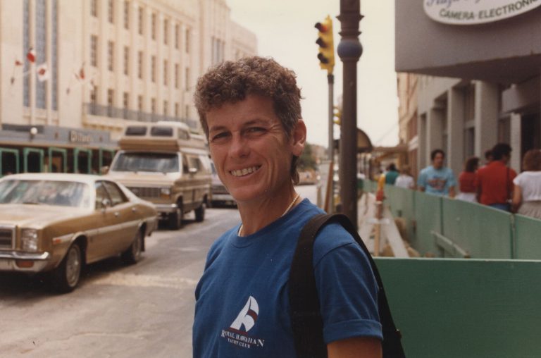 Caylene Caddell smiling at the camera in a blue Royal Hawaiian Yacht Club t-shirt on a city street