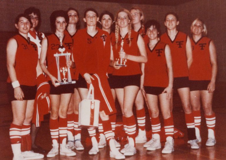 Volleyball team in red uniforms posing with trophies, from the Caylene Caddell collection
