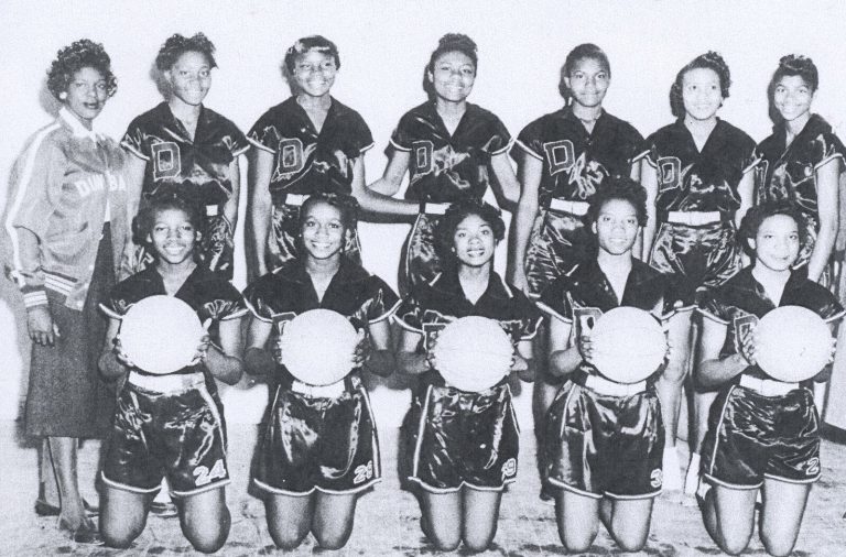 Celestine H. Kyle's Dunbar girls basketball team in dark satin uniforms, with five kneeling players holding basketballs