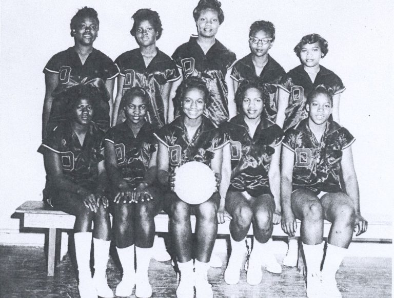 Celestine H. Kyle's Dunbar girls basketball team seated on a bench in dark satin uniforms with a basketball