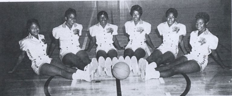 Celestine H. Kyle's Dunbar girls basketball A Team, six players seated on the gym floor around a basketball