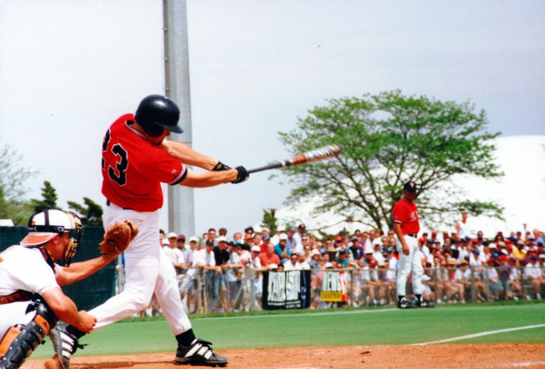Clint Bryant swinging at a pitch in a red Texas Tech jersey with the catcher crouching behind