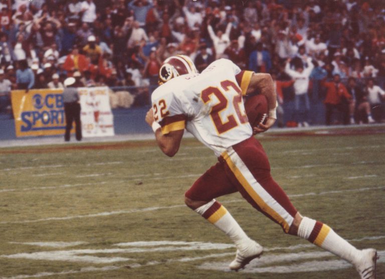 Curtis Jordan, No. 22, running with the football in a white Washington Redskins jersey as fans cheer behind