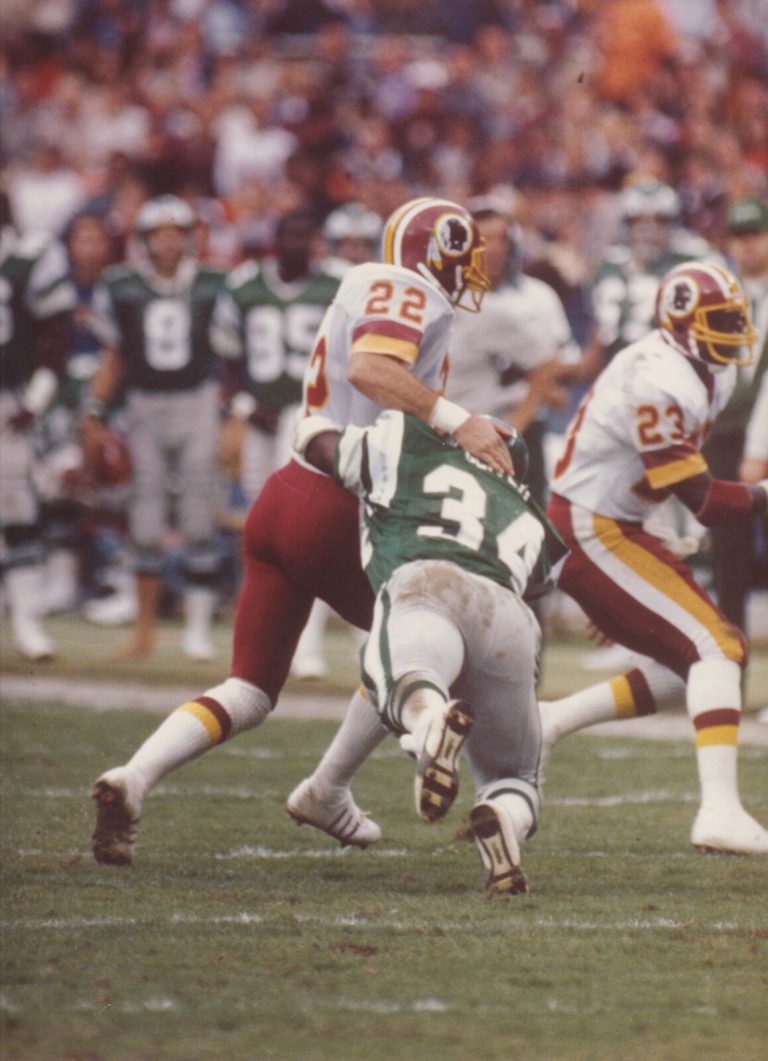 Curtis Jordan, No. 22, in a Washington Redskins uniform blocking a defender in a green No. 34 jersey