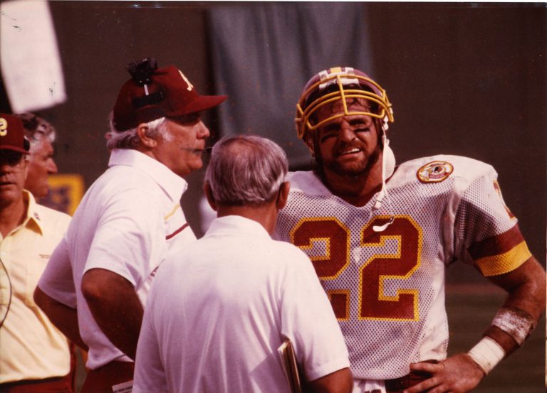 Curtis Jordan, No. 22, in a Redskins helmet and white jersey talking with coaches on the sideline