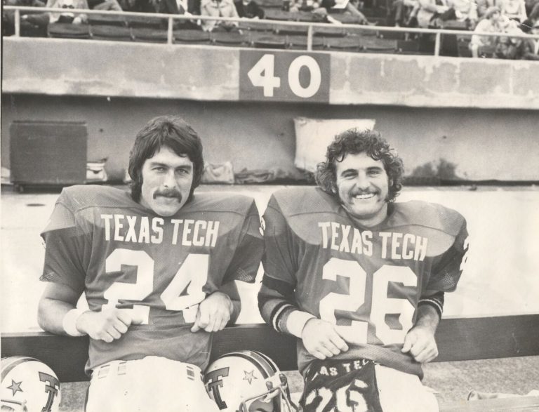 Curtis Jordan and a teammate in Texas Tech jerseys Nos. 24 and 26 smiling on the sideline bench