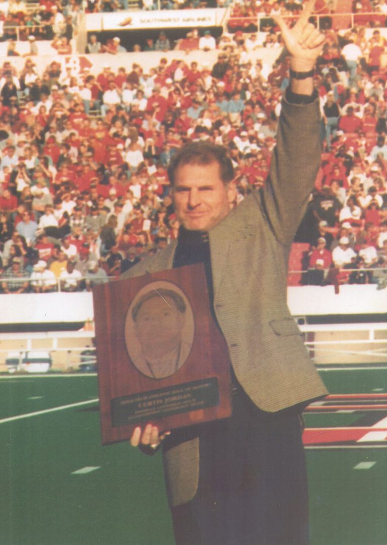 Curtis Jordan holding an engraved plaque and raising an arm to the crowd on a stadium field