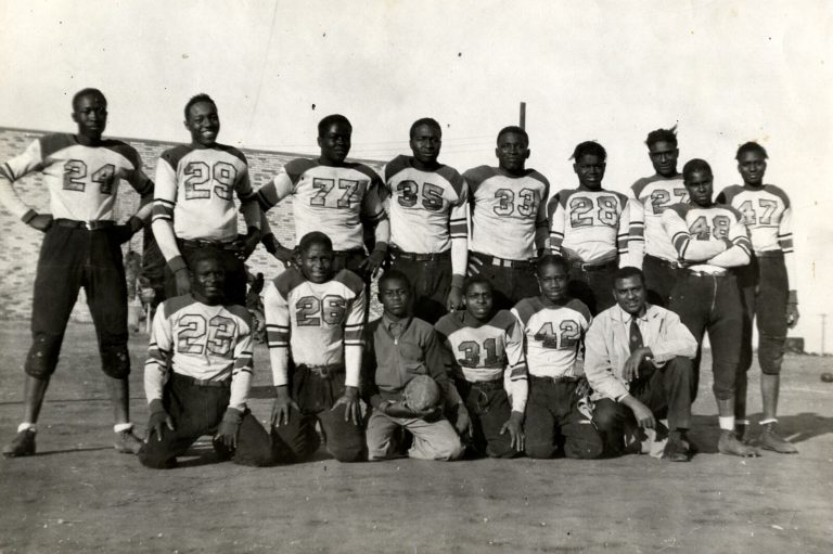 Football team in white jerseys posed outdoors with a man in a tie kneeling at right, from the Damon Hill, Sr. collection