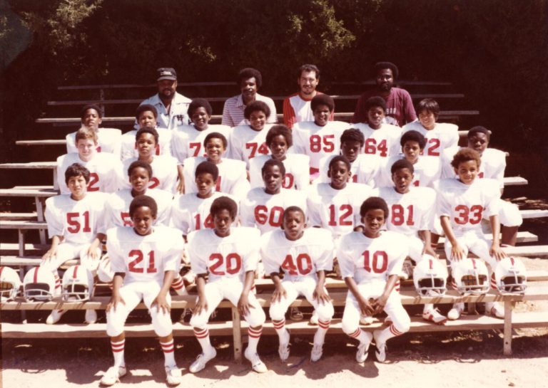 Youth football team in white jerseys with red numbers seated on bleachers with four coaches, Damon Hill, Sr. collection