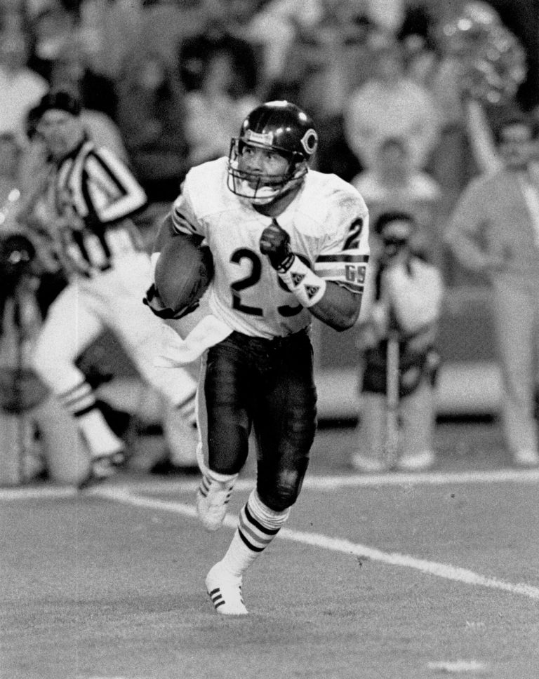 Dennis Gentry, No. 29 for the Chicago Bears, carrying the football as a referee looks on, in a black-and-white photo