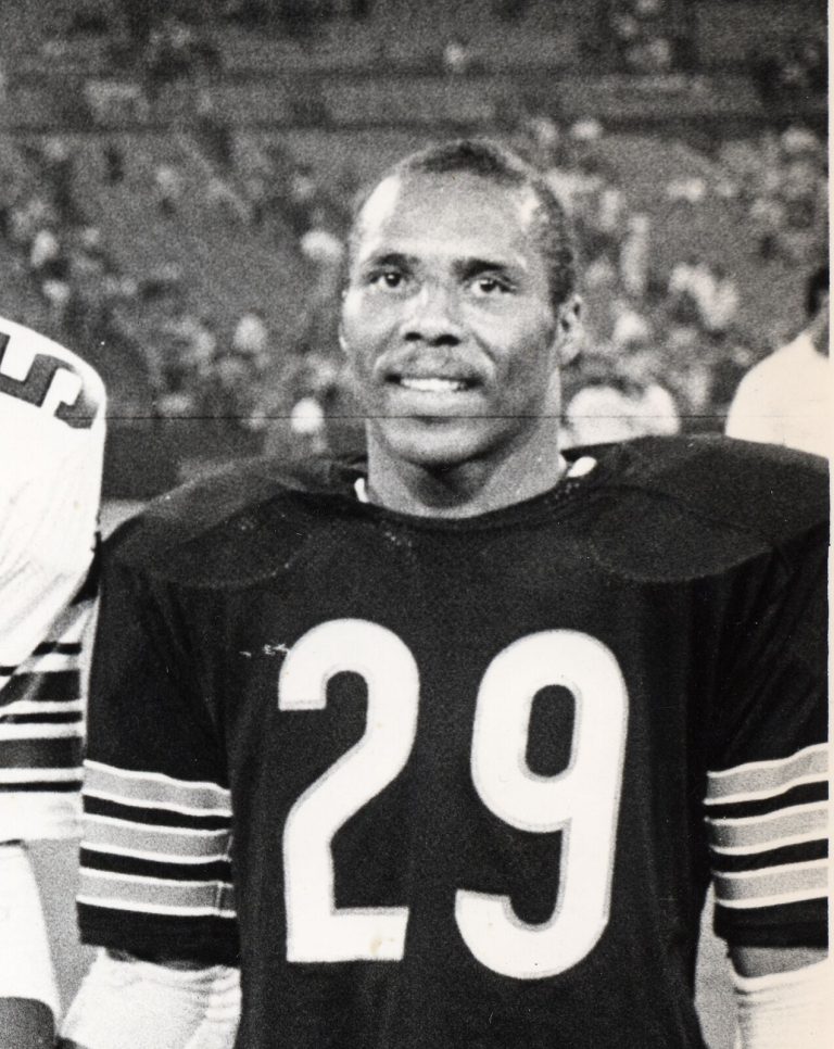 Dennis Gentry smiling in a dark No. 29 Chicago Bears jersey in a black-and-white close-up with a stadium behind