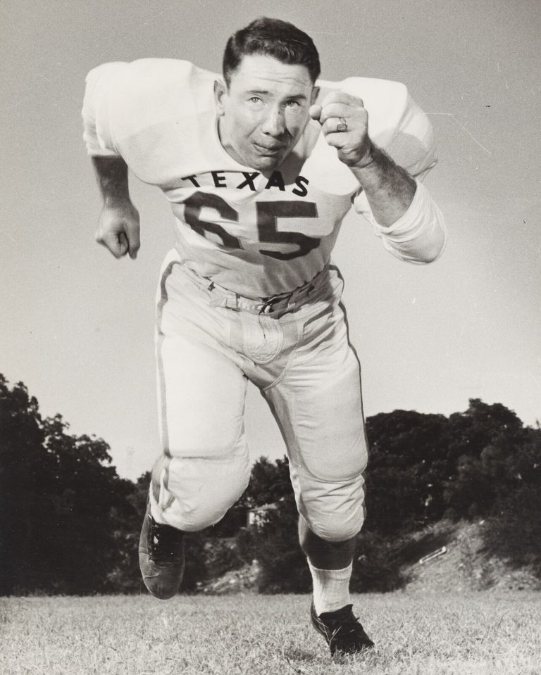 Dick Lowrey in a Texas No. 65 jersey charging toward the camera with a raised fist, black-and-white action pose