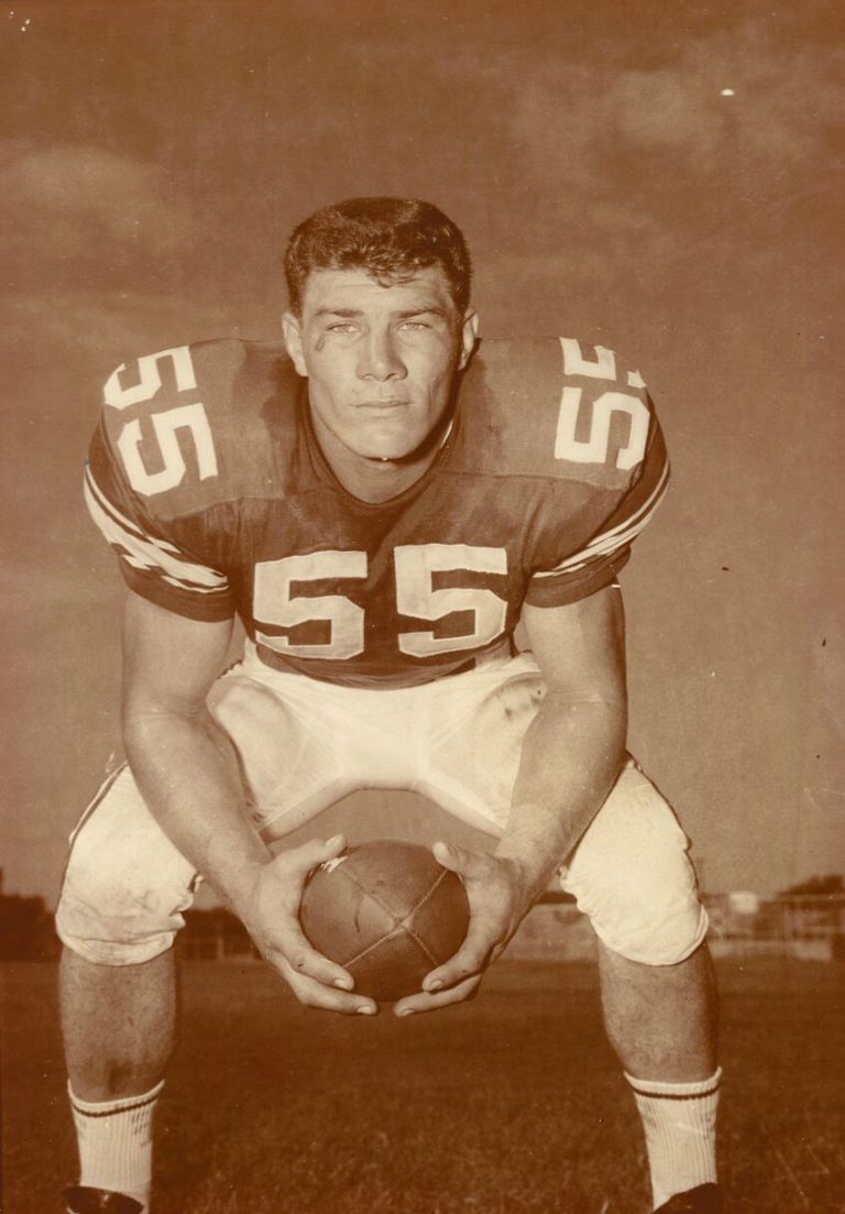 E.J. Holub crouching in a No. 55 jersey and holding a football in a sepia portrait
