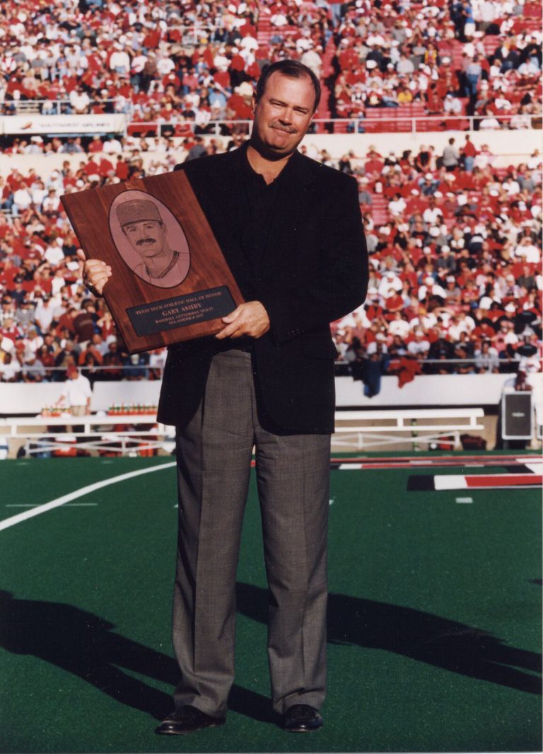 Gary Ashby holding a Texas Tech Athletic Hall of Honor plaque on the field before a packed stadium crowd