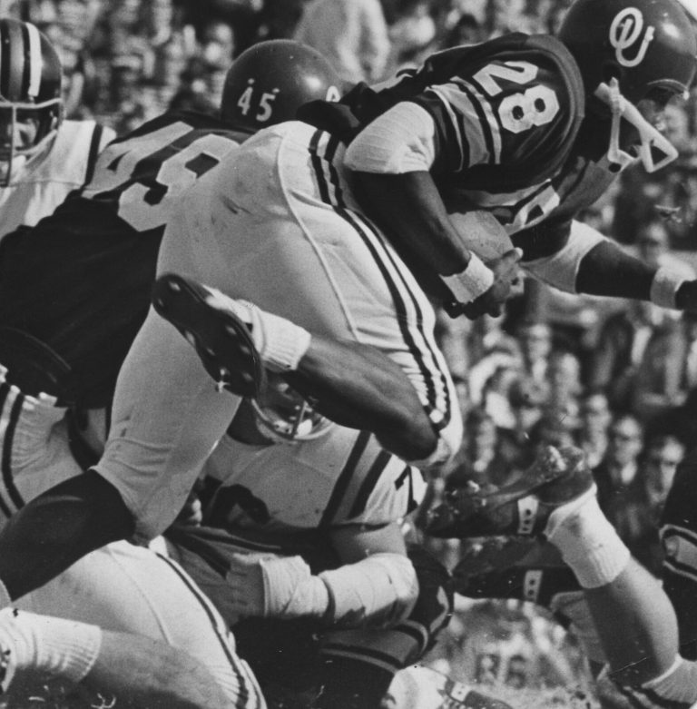 James Ray Jackson, number 28 in an OU helmet, diving forward over a pile of defenders