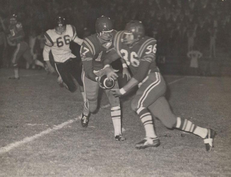 Jerry Austin, No. 36, taking a handoff from the quarterback in a black-and-white night game photo