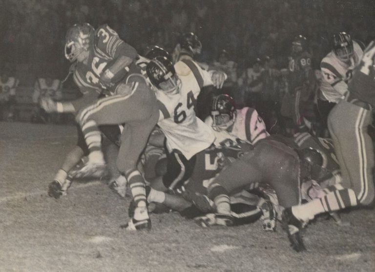 Jerry Austin, No. 36, breaking away from tacklers in a black-and-white night game photo