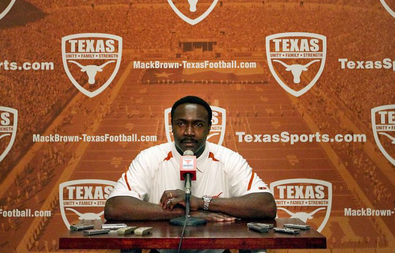 Jerry Gray at a table with a microphone in front of a Texas Longhorns press conference backdrop