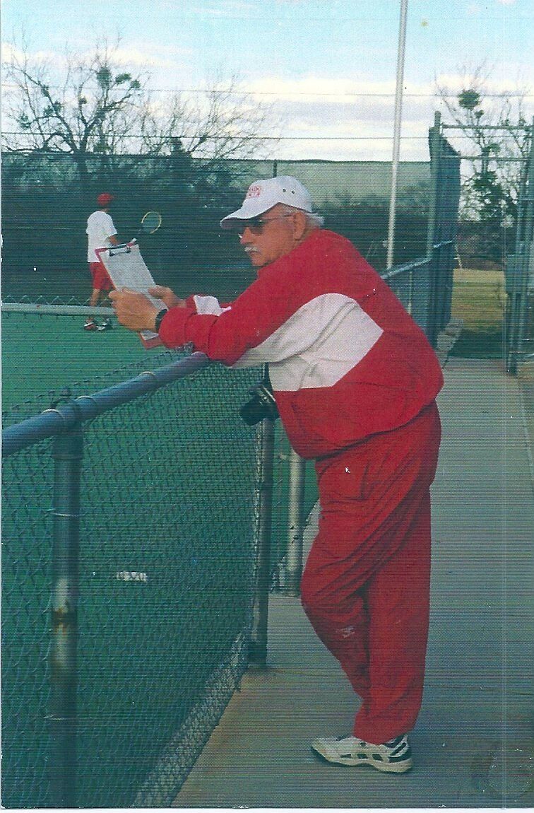 Man in a red warm-up suit and white cap holding a clipboard at a courtside fence, from Jim Carter's collection