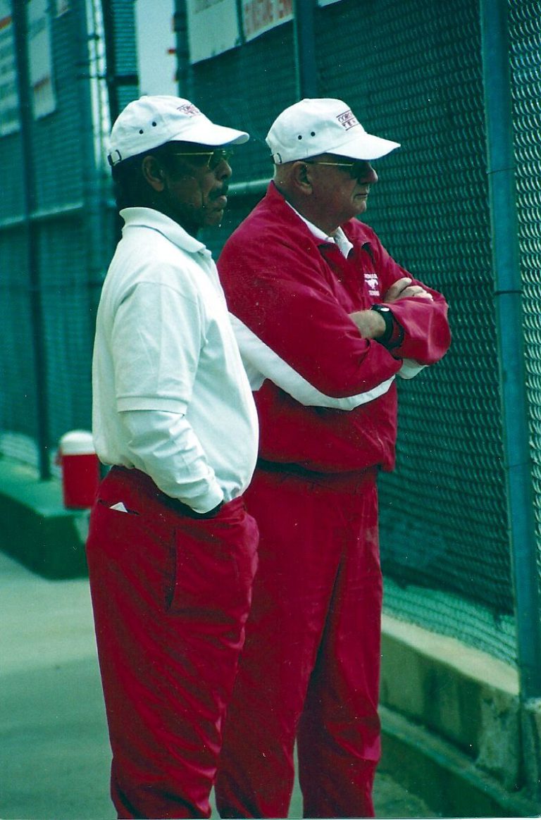Two men in white caps and red tennis warm-ups standing at a fence, from Jim Carter's collection