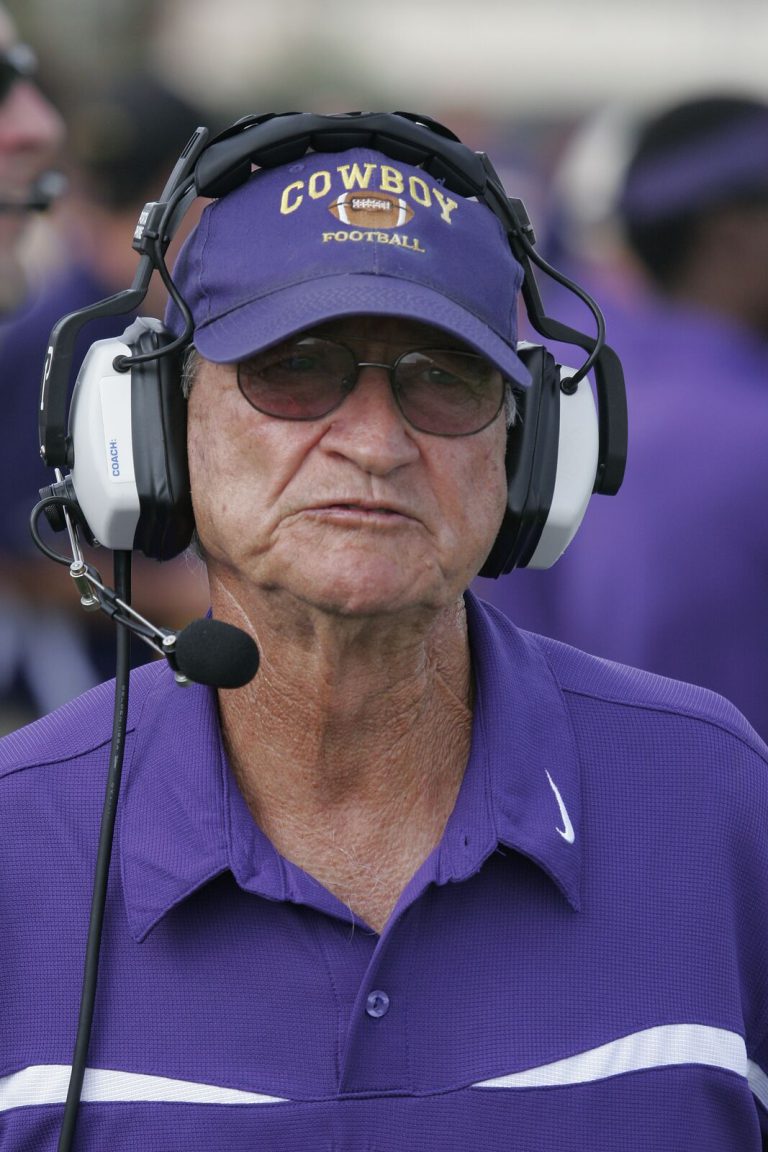 Jimmie Keeling on the sideline in a purple polo, coaching headset and Cowboy Football cap