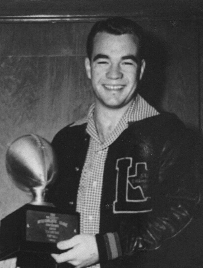 Jimmy Welch smiling in a letter jacket with a large L while holding a football trophy