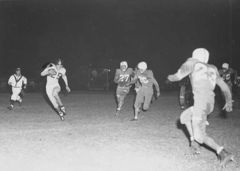 Joe Michalka, number 25, carrying the football past chasing defenders in a night game as a senior