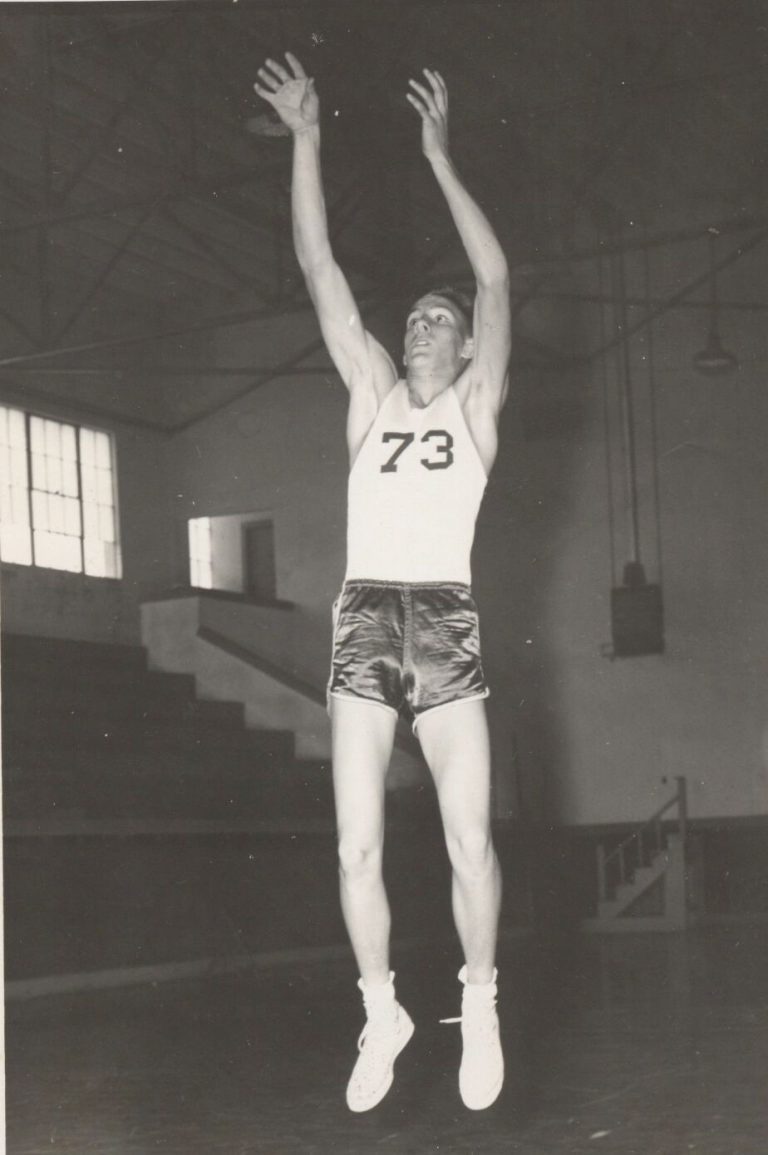 Joe Michalka in a number 73 basketball uniform, leaping with both arms raised in a gym