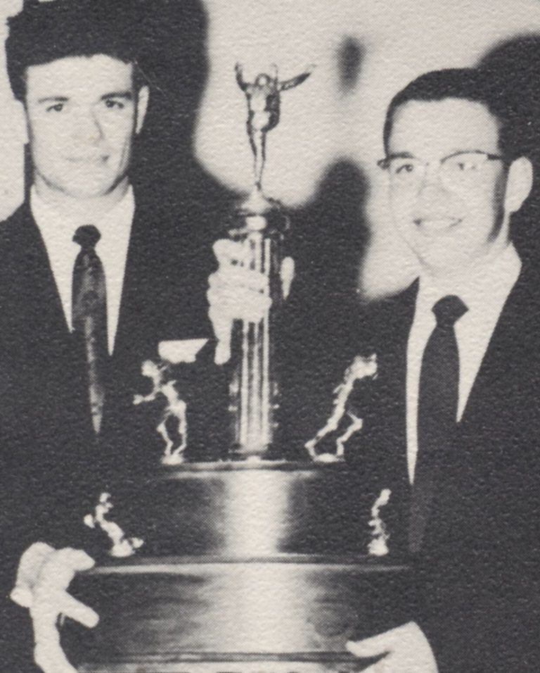 Two men in dark suits holding a large trophy, from the Springlake school scrapbook of John Cardinal
