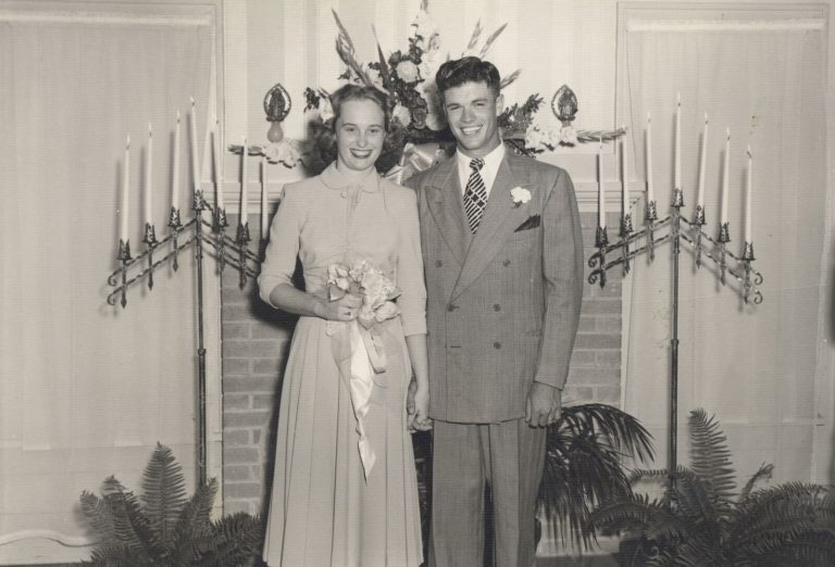 Vintage wedding portrait of a bride and groom in front of tall candelabras, from the John Cardinal family photos