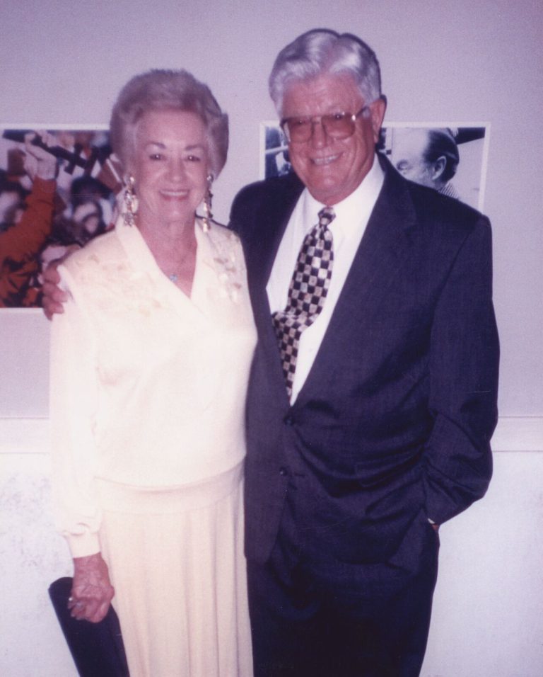 John Cardinal and wife posing together indoors in front of framed photographs