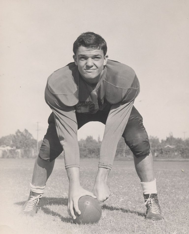 Johnny Tatum bending over a football with both hands on it, posed on a grass field