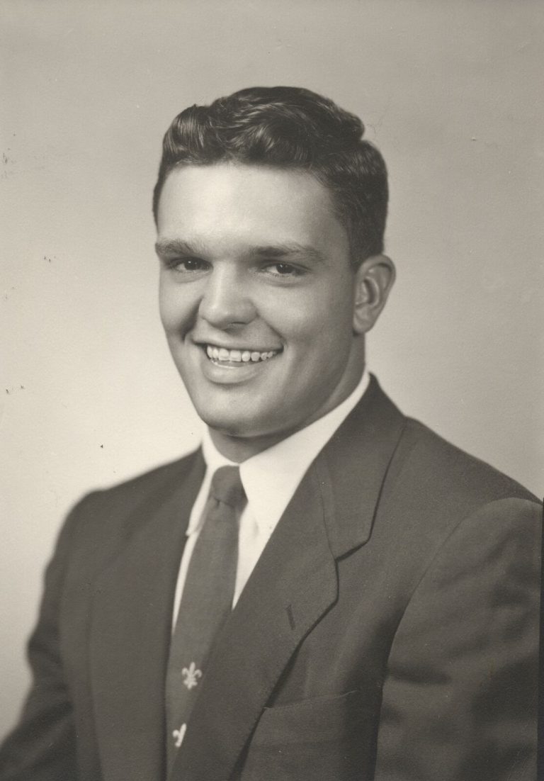 Johnny Tatum smiling in a dark suit and patterned tie, black-and-white studio portrait