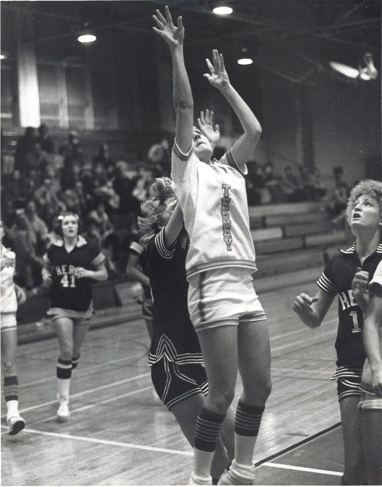 Kamie Ethridge leaping with arms raised for a shot in a Monterey uniform in a black-and-white game photo