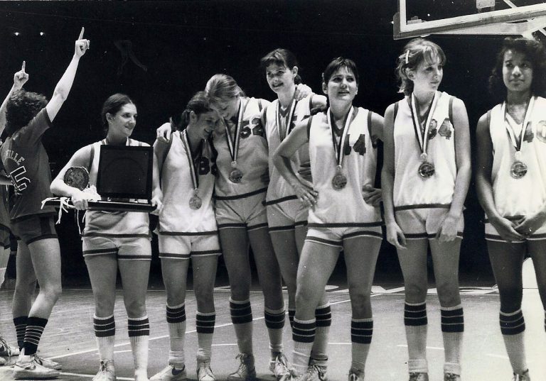 Kamie Ethridge's team in white uniforms wearing medals, one holding a plaque, in a black-and-white photo