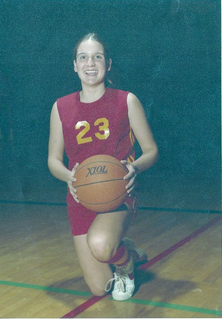 Kamie Ethridge kneeling with a basketball in a maroon No. 23 jersey on a gym floor