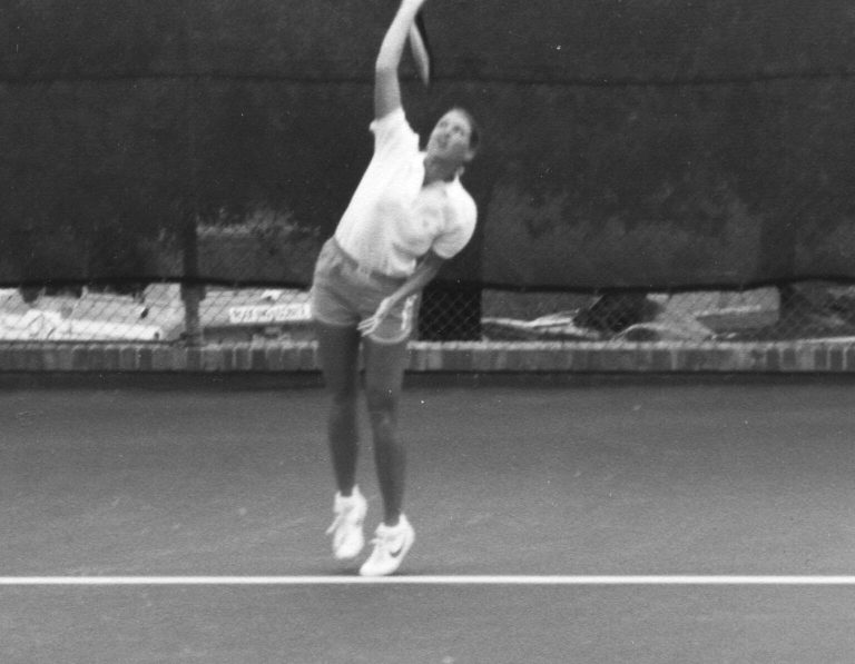 Kathy Kuhne Vick leaping to serve on a tennis court, black and white